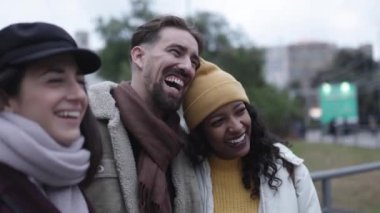 Three happy young multiracial friends laughing together outdoors in city street in winter - Friendship, community and unity concept. High quality 4k footage