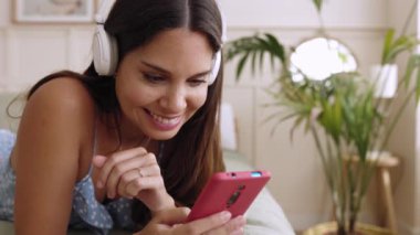 Young beautiful woman relaxing on bedroom lying on bed using smartphone. Slow motion high quality 4k footage