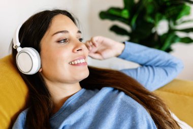 Sıcak evinde kanepede uzanmış gülümseyen bir kadın. Oturma odasında müzik dinlerken kanepede dinlenen mutlu genç bayan.