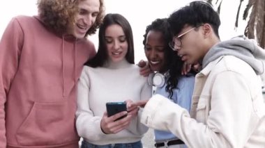 Çok ırklı bir grup genç arkadaş cep telefonunda sosyal medya uygulaması kullanarak eğleniyor. Yüksek kalite 4k görüntü