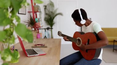 Gülümseyen Afrikalı genç bir kadın evde dizüstü bilgisayar kursunu izlerken akustik gitar çalıyor - E-öğrenme, eğitim ve çevrimiçi sınıflar konsepti