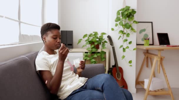 Młoda Afrykanka Jogurt Relaksując Się Kanapie Domu Wysokiej Jakości Materiał — Wideo stockowe