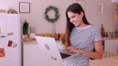 Evde çalışırken dizüstü bilgisayarda yazan gülümseyen beyaz kadın - mutfakta bilgisayar kullanan serbest girişimci kadın - küçük işletme ve telekomünikasyon kavramı