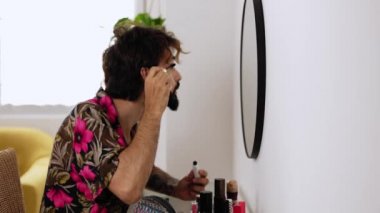 Kirpik süren genç bir adam tuvalet masasında oturuyor. Transseksüel adam evde makyaj yapıyor. LGTBI ve çeşitlilik kavramı. Yüksek kalite 4k görüntü
