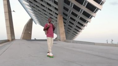 Boş şehir sahnesinde kaykay süren mutlu genç öğrenci. Milenyum Afrikalı Amerikalı genç çocuk dışarıda eğleniyor. Yüksek kalite 4k görüntü