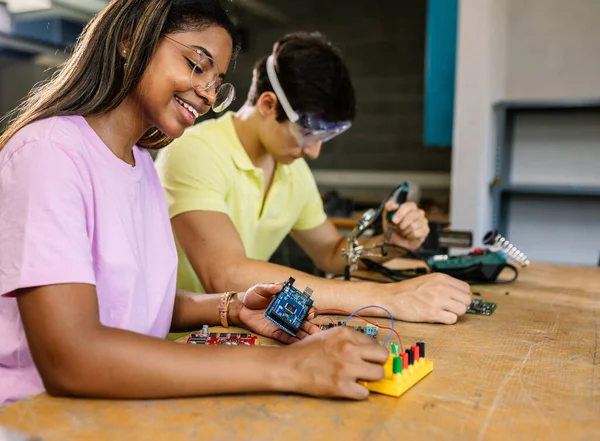 Young diverse students learning together at stem robotics class - Hispanic latin female building electronic circuits at school