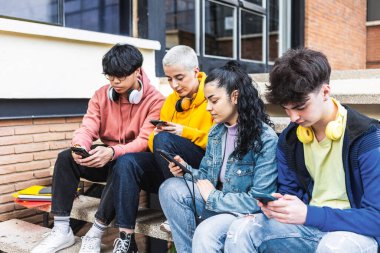 Okul kampüsünde cep telefonu kullanan bir grup genç öğrenci, akıllı telefon cihazıyla sosyal medya uygulamasında sohbet eden yeni moda insanlar. Gençlik ve teknoloji kavramı