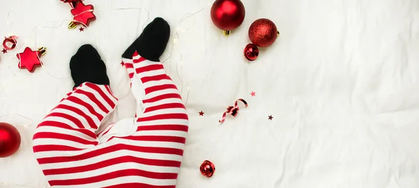 圣诞作文 一个新生婴儿的腿 带着圣诞玩具 背景是白色的床单 圣诞节的背景 小圣诞老人 圣诞节的背景横幅布局 明信片 平躺在床上复制空间 — 图库照片