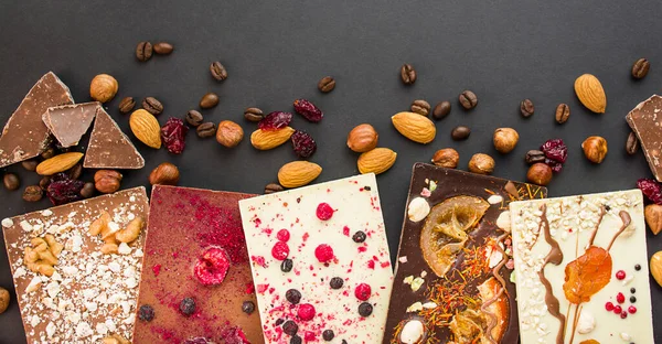 Handmade chocolate with berries, nuts, dried fruits on a dark background. Black and white chocolate. Chocolate bar. Close-up. Chocolate background. Culinary background.