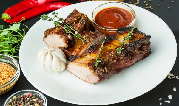 Baked ribs on a white dish. Grilled ribs with spices and herbs on a dark background. Food background.Close-up.
