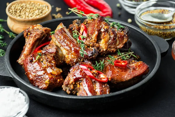 Baked ribs in a pan. Roasted pork ribs with spices and herbs on a dark background. Food background. Side view. Close-up.