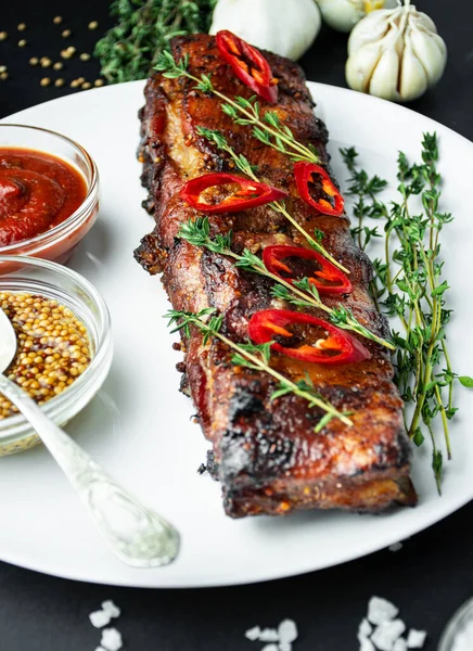 Baked ribs on a plate. Roasted ribs with spices and herbs on a dark background. Food background. Side view. Close-up.