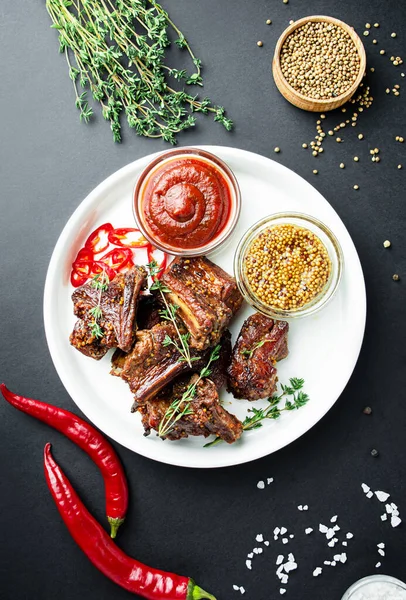 Baked ribs. Roasted pork ribs with spices and herbs on a dark background. Food background. View from above. Copy space.