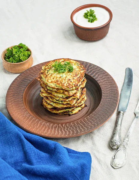 Zucchini fritters, vegetarian zucchini pancakes, served with fresh herbs and sour cream, top view. Light background.