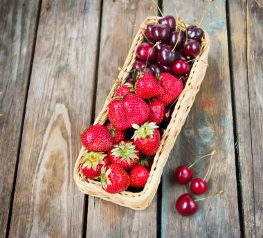 çilek ve tatlı kiraz ahşap bir masa üzerinde gerdanlı sepet içinde