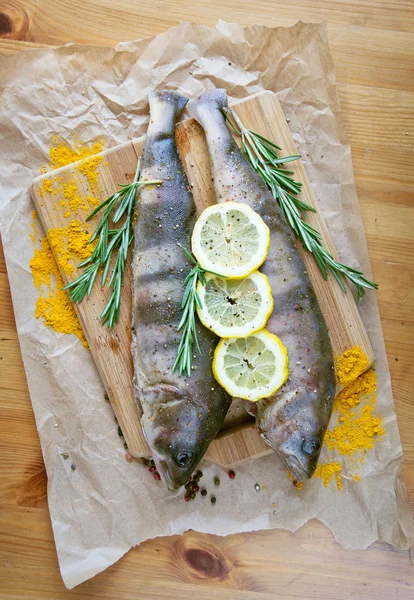 Fresh fish on wooden kitchen board with, rosemary, lemon and colorful peppercorns on wooden background. Culinary healthy cooking. — Stock Photo, Image