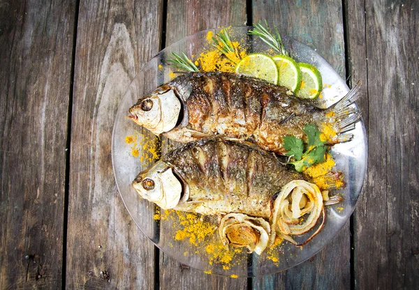 A friss fűszernövények és a citrom, a fából készült asztal két sült halat — Stock Fotó