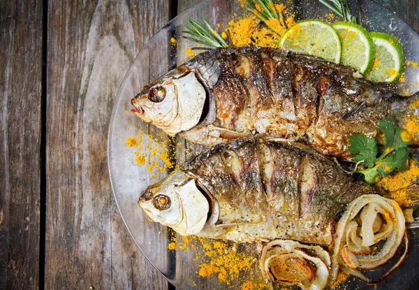 Two fried fish with fresh herbs and lemon on wooden table — Stock Photo, Image