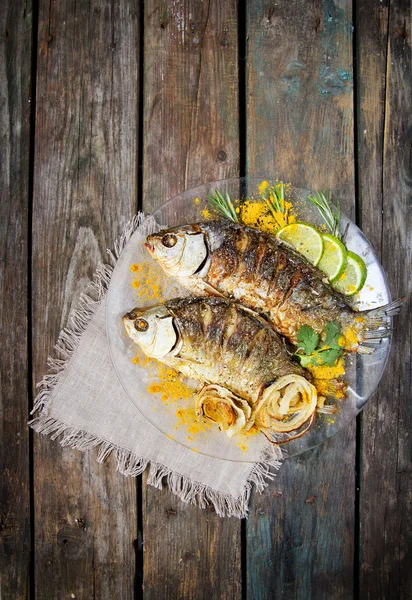 与新鲜的药草和柠檬木制的桌子上的两个煎的鱼 — 图库照片