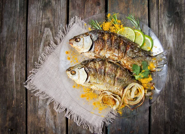 Two fried fish with fresh herbs and lemon on wooden table — Stock Photo, Image