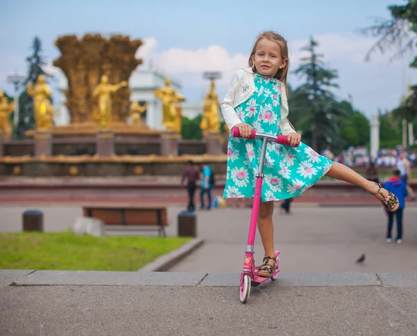 Menina da criança bonito alegre na scooter em um parque — Fotografia de Stock