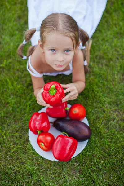 Bambina con le treccine in un giardino con un piatto di verdure — Foto Stock