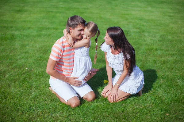 Jeune famille de trois personnes s'asseoir sur l'herbe et s'amuser — Photo