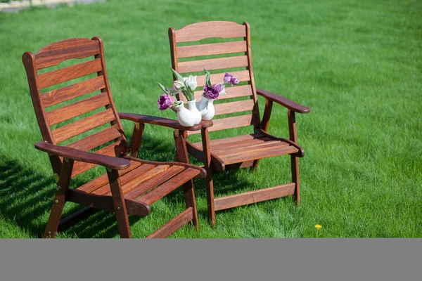 Duas cadeiras de madeira na grama com vaso de flores sobre eles — Fotografia de Stock