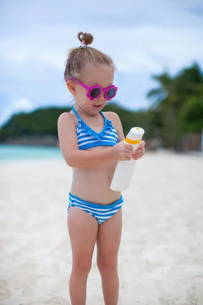 Piccola adorabile ragazza in costume da bagno tiene bottiglia lozione abbronzatura — Foto Stock