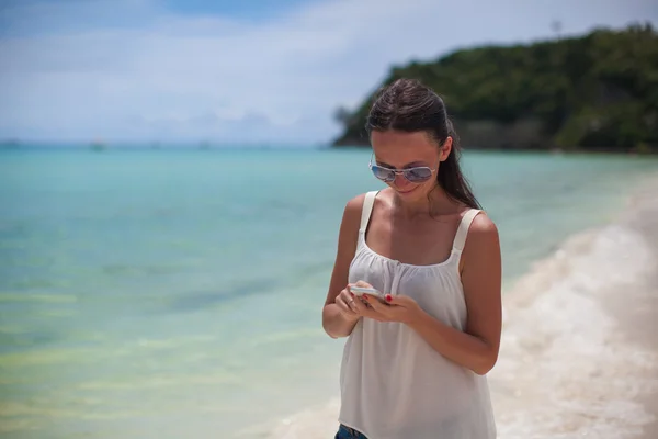 Jovem mulher bonita na praia olhando em seu telefone — Fotografia de Stock