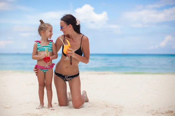 Happy mother and her adorable little daughter with juice at tropical beach — Stock Photo, Image