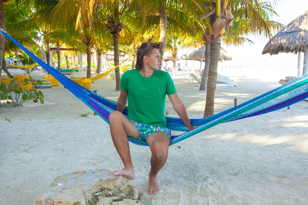 Young man sitting in hammock on the beach and looking at the sea — Stock Photo, Image