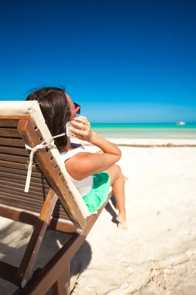 Młoda kobieta rozmawia przez telefon, siedząc na leżaku plaża — Zdjęcie stockowe