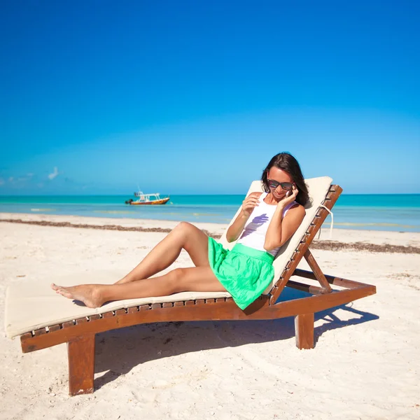 Mode vrouw praten over de telefoon zittend op een strand ligstoel — Stockfoto