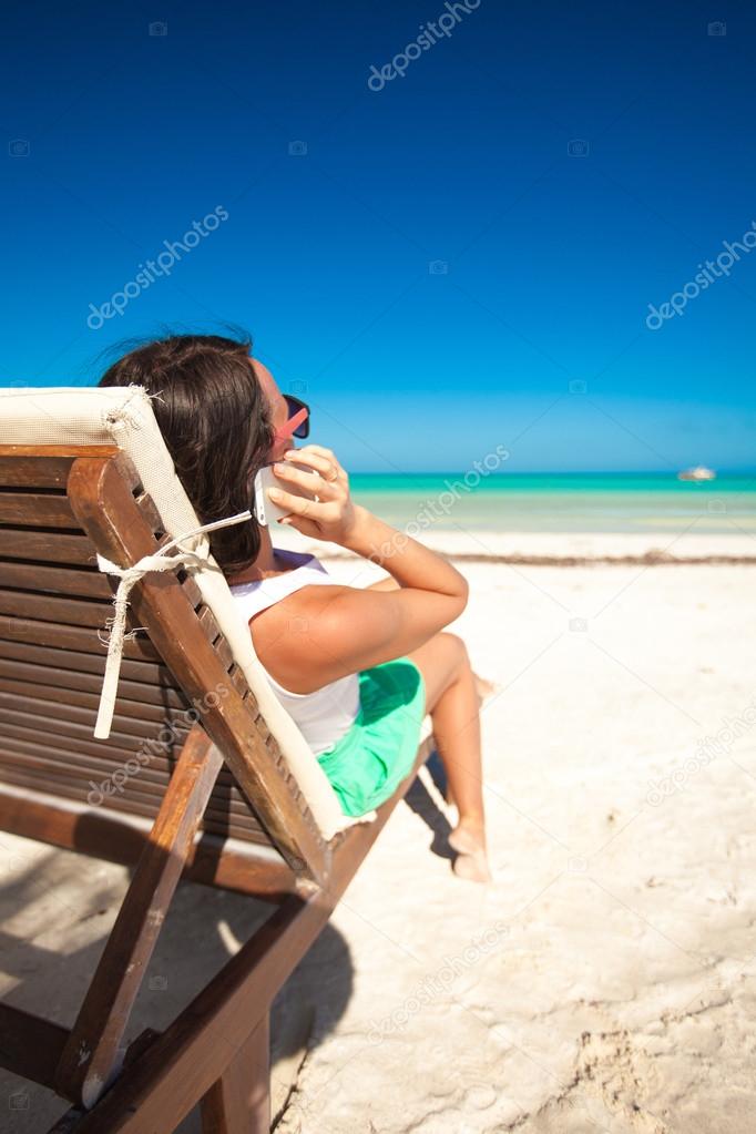 Young woman talking on the phone while sitting on a beach lounger