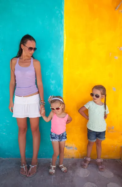 Young mother with cute daughters standing near bright colored wall — Stock Photo, Image