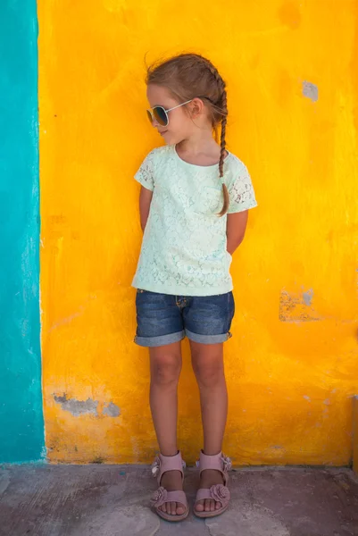 Piccola ragazza carina in piedi vicino alla parete colorata brillante — Foto Stock