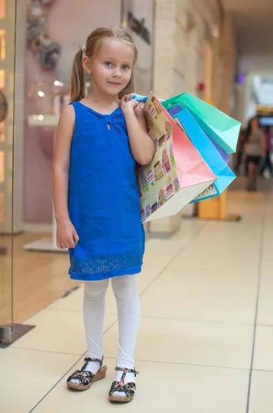 Little fashion girl with packages in a large shopping center — Stock Photo, Image