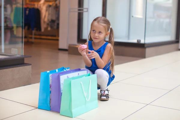 Pequeña chica de la moda se sienta cerca de paquetes en un gran centro comercial — Foto de Stock
