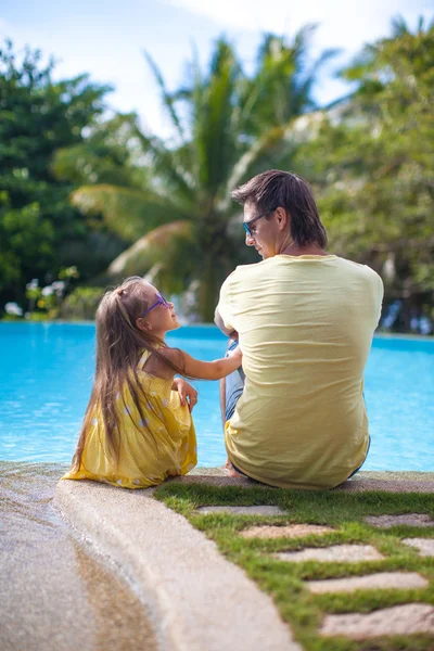 Back view of a young father and his cute daughter sitting near the swimming pool — Stock Photo, Image