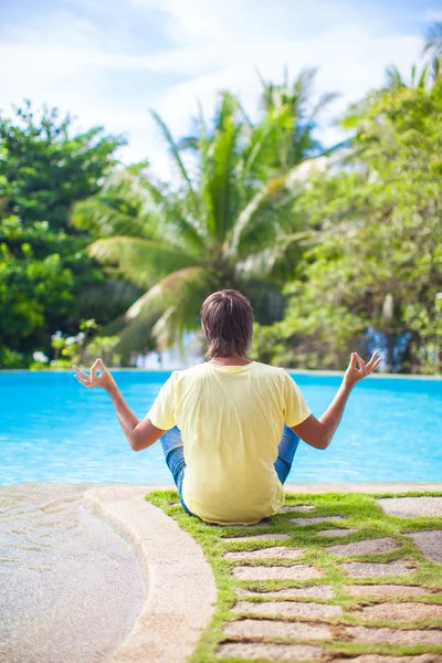 Young man sitting in the lotus position near the swimming pool — Stock Photo, Image