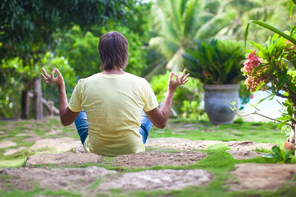 Junger Mann sitzt in Lotusposition im Garten in wunderschönem Ferienort — Stockfoto