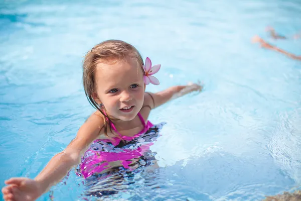 Pequeña linda chica feliz con flor detrás de su oreja se divierte en la piscina — Foto de Stock