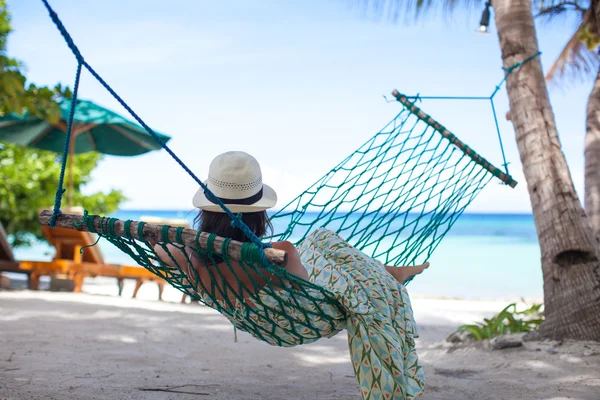 Donna in cappello sdraiata in amaca all'ombra di un albero su una spiaggia — Foto Stock