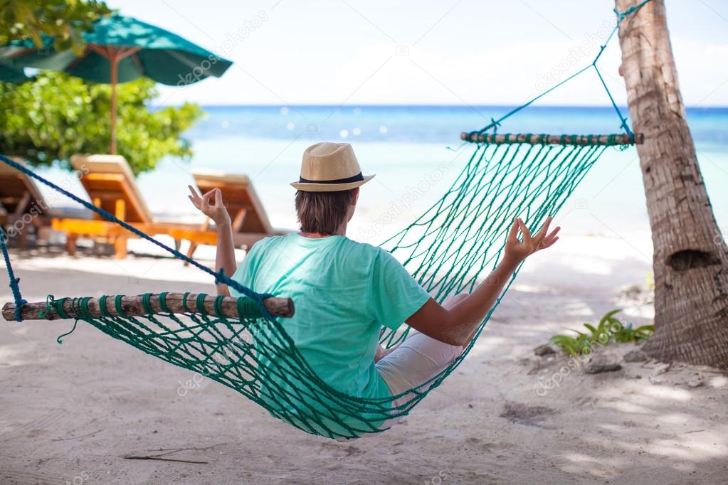 Young man sitting in hat in the lotus position in hammock