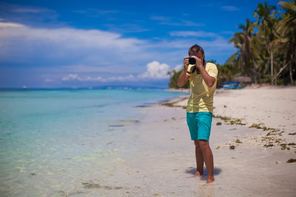 Vor der Kamera junger Mann mit Kamera in der Hand am schönen weißen Sandstrand — Stockfoto