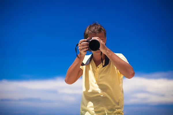 In front of the camera young man with camera in hands background the blue sky — Stock Photo, Image