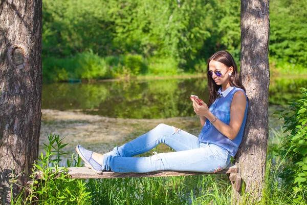 屋外に座っていると、携帯電話を見て若い女性 — ストック写真