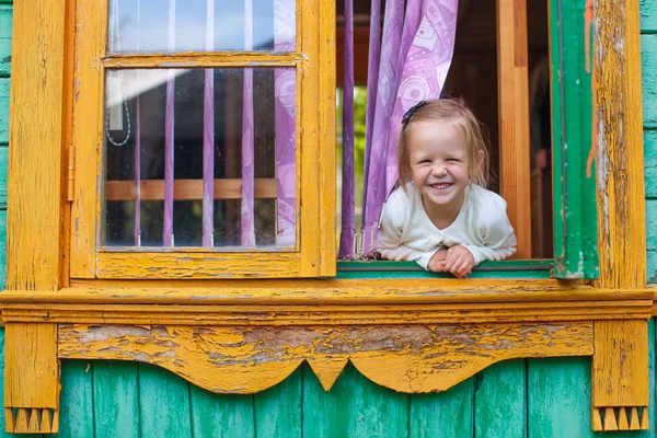 Adorable little girl looks out the window rural house and laughs — Stock Photo, Image