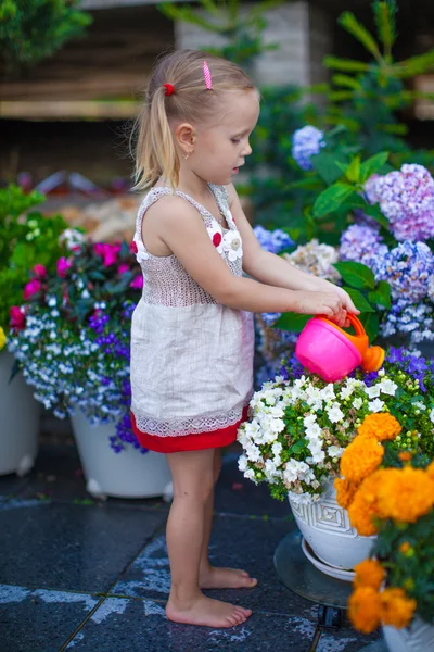 Маленькая милая девочка поливает цветы лейкой банкой — стоковое фото